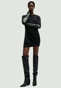 Robe mini noire à manches longues avec des détails froncés, associée à des bottes noires montantes élégantes et des gants noirs texturés.