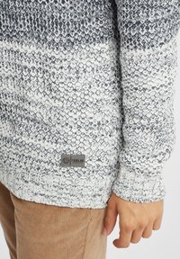 Gestrickter Pullover in Grau und Weiß mit einem strukturierten Muster. Verfügt über ein Etikett am Saum, gerippte Bündchen und einen lässigen Schnitt.