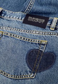 Lichtblauwe denim jeans met een hartvormige patch op de achterzak, voorzien van gele stiksels en een zwart label met de tekst "Fabienne Chapot."