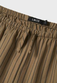 Tissu rayé marron avec une surface texturée, comportant une taille élastique et une étiquette "LMTD". Les rayures sont foncées sur le fond marron.