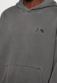 Harmaa huppari, pehmeästä kankaasta, jossa on kengurun tasku ja hillityt kirjotut eläinaiheet rinnassa. Tavallinen huppuosan malli.