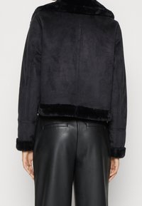 Svart mockajacka i cropped modell med en mjuk krage och manschetter i syntetpäls, med en slät yta och minimalistisk design. Bärs över svarta läderbyxor.