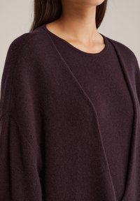 Üks suurus sobib kõigile tumepunane kampsun, millel on ümar kaelus ja langenud õlavarred, pehme tekstuur ja mugav istuvus.