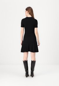 Black ribbed dress with a flared hemline, short sleeves, and a collared neckline. Paired with knee-high black heeled boots.