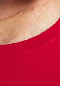 T-shirt in cotone rosso con scollatura a girocollo a coste, texture liscia e cuciture visibili lungo il colletto e l'area delle spalle.