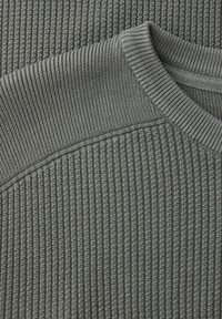 Pull en maille côtelée grise avec une surface texturée, un col rond et un col lisse contrastant. Tissu durable au toucher doux.