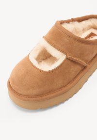 Brune mokkasiner i semsket skinn med rund tå, plysjinnredning, borrelåsrem og en beige gummisåle. Åpen design over vristen.