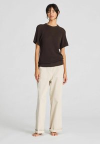 Top marrone a maniche corte con scollatura rotonda, abbinato a pantaloni larghi beige chiaro con tasche frontali e orli arrotolati. Design minimalista.