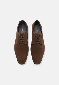 Chaussures habillées en daim marron avec une finition lisse, présentant un bout arrondi et un laçage à trois œillets. La doublure présente une couleur contrastée.