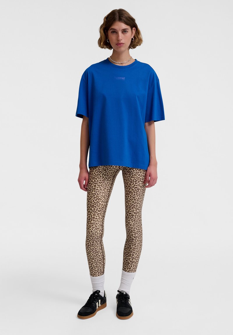 Blå oversized t-shirt med rund hals och subtil logotyp, tillsammans med figurnära leopardmönstrade leggings och svarta sneakers med strukturerad sula.