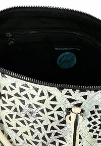 Bolso Gabs con un patrón geométrico texturizado en crema y negro, que incluye un cierre de cremallera, un bolsillo interior y una etiqueta de marca azul.