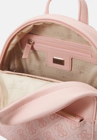 Petit sac à dos rose en faux cuir. L'intérieur présente un revêtement beige avec un motif de logo répété, une poche zippée et un compartiment principal.