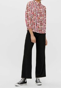 Blouse à manches courtes avec un motif abstrait multicolore en rose, rouge et blanc, associée à un pantalon noir à jambes larges et des baskets noires.