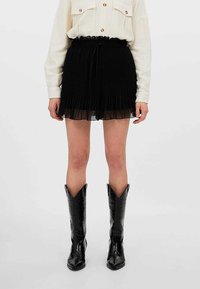 Czarna plisowana mini spódniczka z marszczonym pasem i przezroczystą nakładką. Noszona z wysokimi czarnymi kowbojkami o fakturze krokodyla.