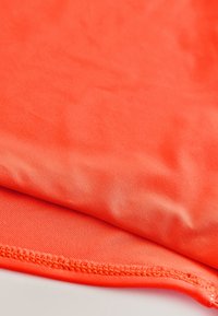 Tissu orange vif avec un bord replié montrant une couture serrée et régulière le long de l'ourlet.