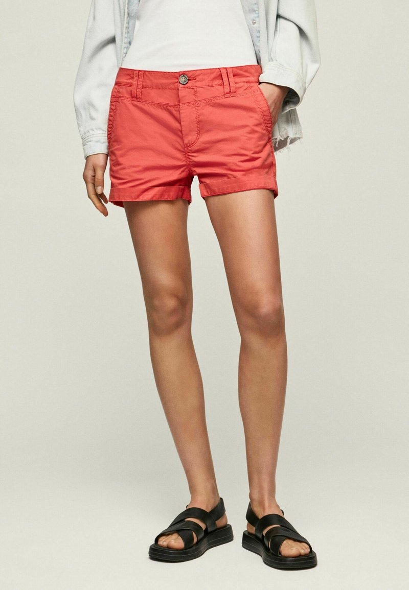 Shorts en coton rouge à coupe décontractée, avec une fermeture à boutons sur le devant et des poches latérales. Associés à des sandales noires à lanières.