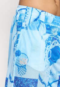 Blå mesh basketballshorts med et abstrakt mønster, elastisk talje og logo-patch. Teksturen er åndbar og letvægtig.