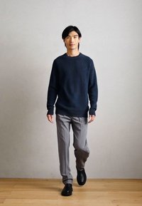 Pulover bleumarin cu model texturat, pantaloni gri deschis și încălțăminte neagră. Ansamblul are o croială lejeră și texturi netede, potrivit pentru medii casual.