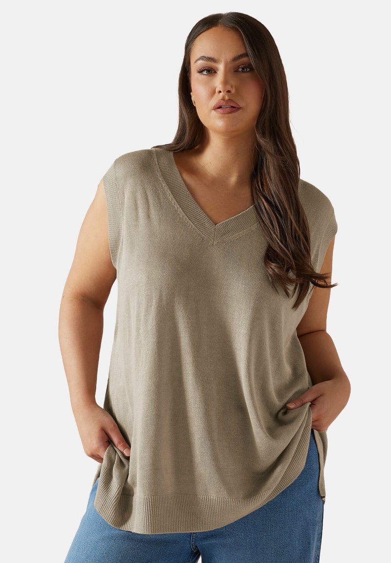 Ljusgr�ön ärmlös topp med v-ringning, tillverkad av strukturerad tyg, med lös passform och sidofötter, ihop med blå jeans.