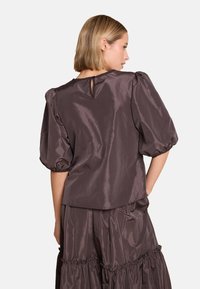 Mørkebrun satengbluse med pufferm og detalj med nøkkelhull bak. Glatt tekstur, avslappet passform og samlede detaljer ved kanten.