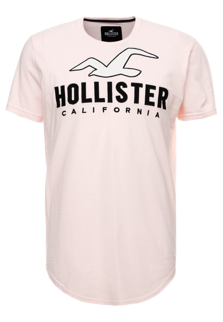 Ljust rosa bomullströja med korta ärmar, med en svart "HOLLISTER"-logotyp och texten California i fet stil. Rundad nederkant.