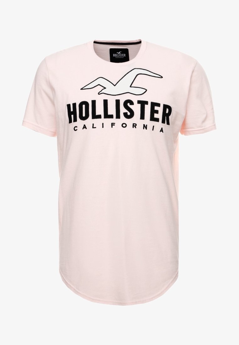 Ljust rosa bomullströja med korta ärmar, med en svart "HOLLISTER"-logotyp och texten California i fet stil. Rundad nederkant.