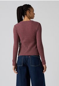 Maglietta a maniche lunghe di maglia borgogna con un motivo testurizzato, caratterizzata da un collo rotondo e una silhouette aderente. Abbinata a pantaloni in denim a gamba larga.