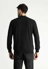 Maglione nero in cotone con maniche lunghe, collo rotondo, polsini e bordo a coste. Presenta una texture liscia e una vestibilità comoda, mostrato da dietro.