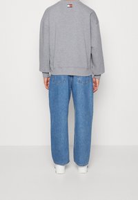 Šedá mikina s pohodlným střihem, žebrovanými manžetami a lemem. Doplňena světle modrými volnými džínami s dvojitými kapsami a rovnými nohavicemi.