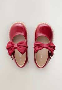Scarpe in pelle verniciata rossa con finitura texture, punta rotonda e grandi fiocchi a costine. Presentano una cinghia con chiusura a fibbia e suola beige.