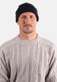 Bonnet en tricot noir et pull en tricot torsadé gris clair avec des motifs texturés. Le pull présente un col côtelé et des détails en câble sur les manches.