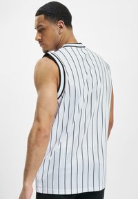 Hvid ærmeløs trøje med sorte lodrette striber, rund halsudskæring og kontrastkant. Stoffet ser åndbart og letvægts ud.