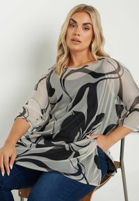 Top leggero e trasparente con un design fluido caratterizzato da motivi astratti in bianco e nero. Collo rotondo e maniche a tre quarti.