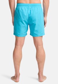 Τιρκουάζ μαγιό με ελαστική μέση και πλαϊνές τσέπες. Κατασκευασμένα από ελαφρύ, λείο ύφασμα, φτάνουν λίγο πάνω από το γόνατο.