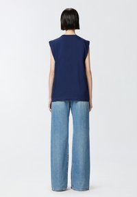 Mornarice plava bezrukavna majica s okruglim izrezom, u kombinaciji s svijetloplavim trapericama visokog struka širokih nogavica koje imaju izblijedjeli izgled.