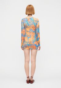 Διάφανο, μίνι φόρεμα με μακριά μανίκια σε μπλε, πορτοκαλί και κίτρινο αφηρημένο σχέδιο. Διαθέτει άνοιγμα στην πλάτη και εφαρμόζει στενά στο σώμα.