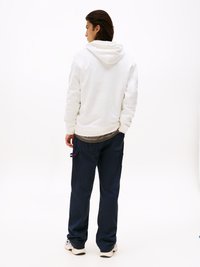 Sudadera blanca con capucha y corte relajado, combinada con pantalones cargo de color azul marino oscuro. Textura lisa, vista trasera que muestra detalles de costura y bolsillos.