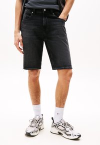 Svarte denimshorts med rett snitt, fem lommer og en ren kant. Båret med hvite sokker og joggesko, som viser en uformell stil.