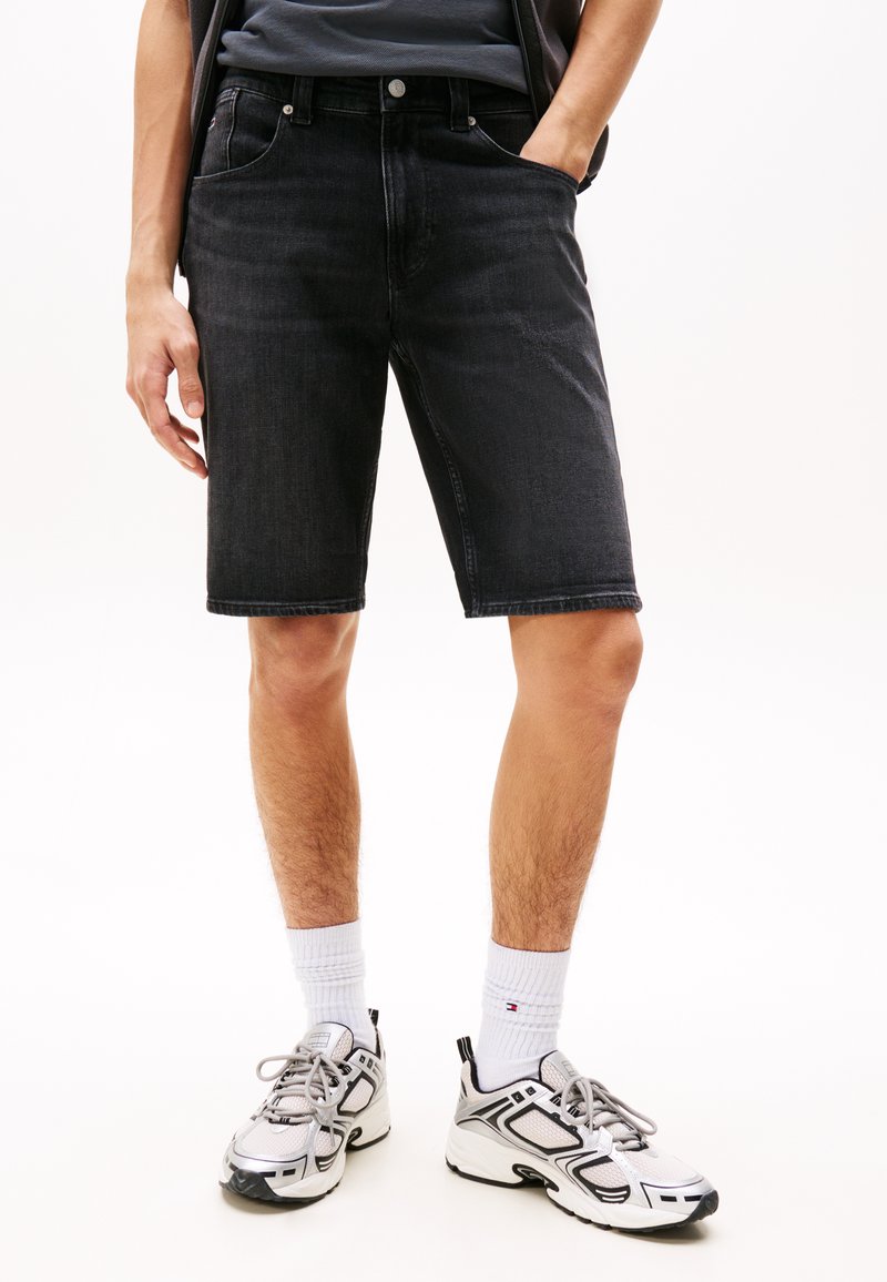 Svarte denimshorts med rett snitt, fem lommer og en ren kant. Båret med hvite sokker og joggesko, som viser en uformell stil.