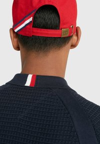 Röd keps med vita och blå ränder, bronshardware, marinblå strukturpolo med en kontrasterande krage i röd, vit och blå.