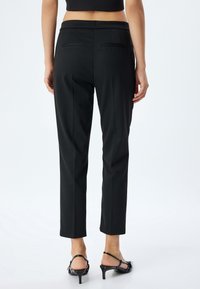 Zwarte, op maat gemaakte broek met een slim fit, voorzien van twee achterzakken, een gladde textuur en een cropped lengte boven de enkels.