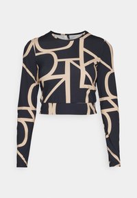 Langermet croppet topp laget av elastisk stoff, med svart base og store, lys beige geometriske mønstre samt rund hals.