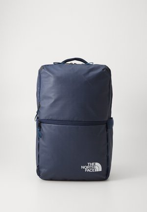 Navy blue backpack made of durable fabric, featuring a front zip pocket, top handle, and the North Face logo in white. Smooth texture.