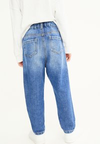 Pantaloni in denim azzurro chiaro con vestibilità rilassata, vita elastica e due tasche posteriori. Presentano aree sbiadite e orli risvoltati.