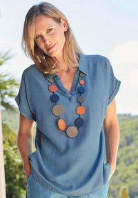 Blaues Kurzarmbluse aus Denim mit Kragen, kombiniert mit einer bunten runden Perlenkette, die orangefarbene, blaue und graue Akzente aufweist.