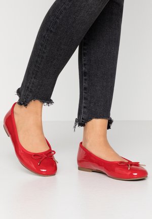 Ballerines rouges en cuir verni avec un bout arrondi et un détail nœud. Associées à un jean noir effiloché, offrant un look décontracté.