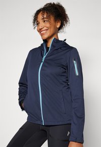 Giacca softshell navy con zip frontale blu e dettagli delle tasche. Presenta un cappuccio regolabile e un tessuto leggero e testurizzato.