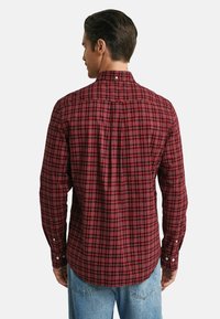 Man wearing a fitted red and black checkered long-sleeve shirt viewed from the back, paired with light blue jeans.