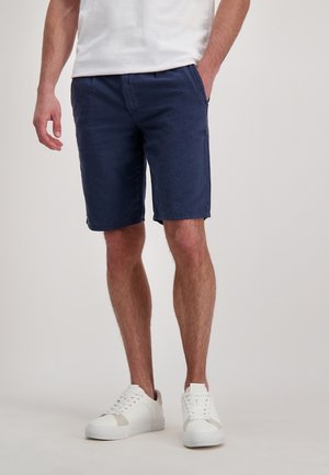 Marineblauwe katoenen shorts met zijzakken, een rechte snit en een gladde textuur. Gepaard met witte sneakers met een gestructureerde zool.