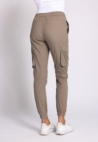 Beige Cargo-Hosen mit elastischem Bund, zulaufenden Beinen und Seitentaschen. Sie zeichnen sich durch eine glatte Textur und eine lässige Passform aus und werden mit weißen Turnschuhen kombiniert.